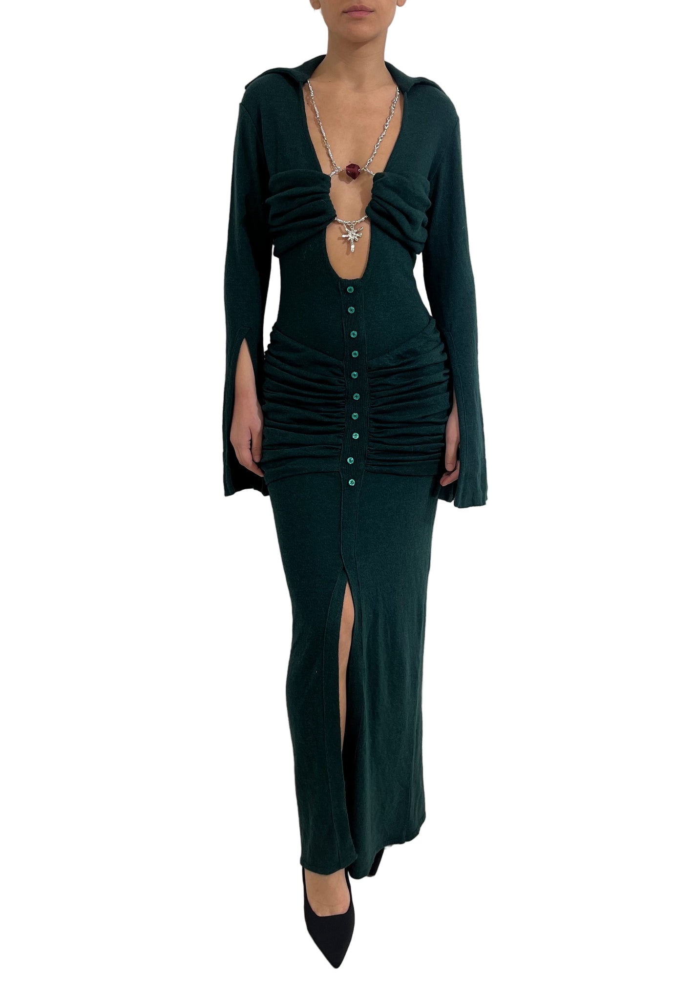 Person wearing a dark green dress with a slit on a plain background